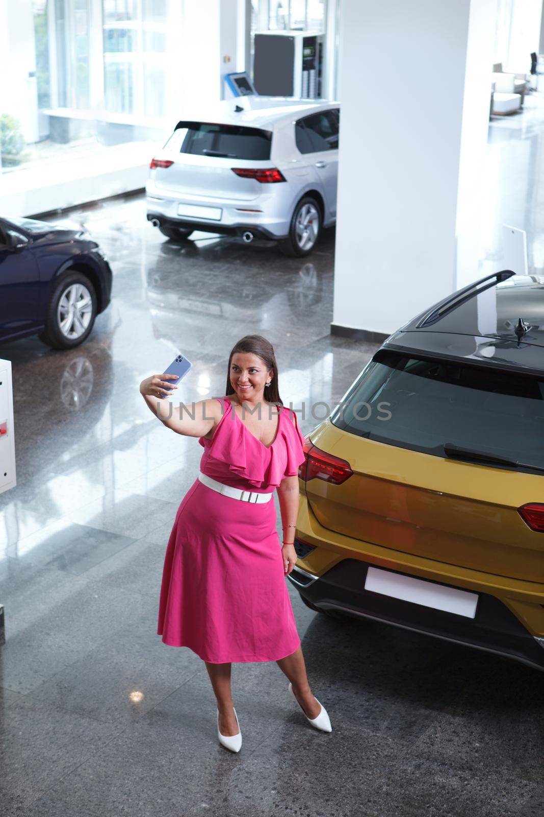 Vertical top view shot of a woman taking selfies with smart phone at car dealership