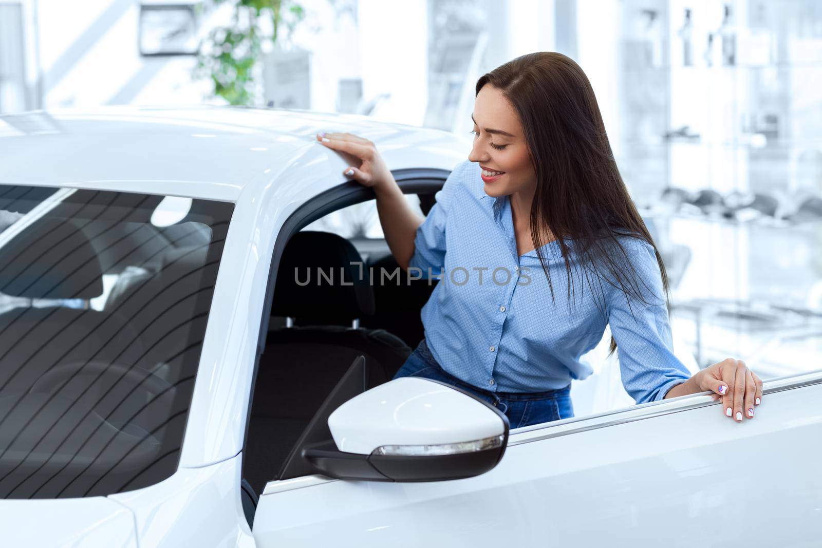 Getting her own car! Beautiful young happy woman getting inside of a new car she is going to buy at the local car salon