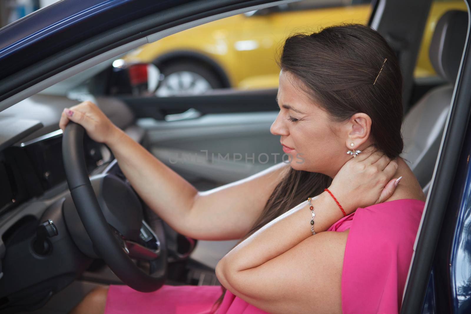 Female driver rubbing her hurting neck, sitting in a car