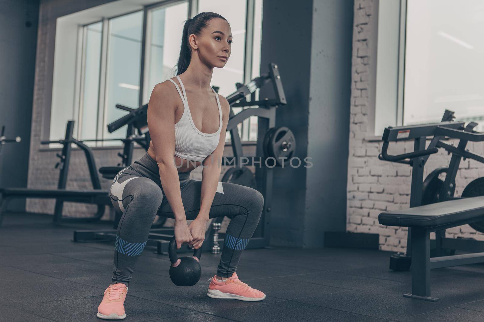Low angle shot of a beautiful sportswoman working out with kettlebell at the gym, copy space. Gorgeous female crossfit athlete doing squats with kettlebell at sports studio. Strength concept
