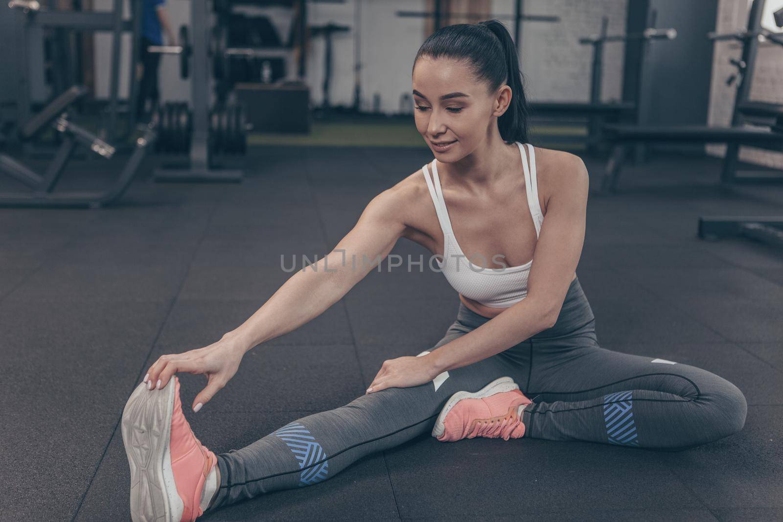 Gorgeous female gymnast stretching her legs at the gym studio, copy space. Full length shot of a beautiful sportswoman warming up before exercising. Flexibility, gymnastics, motivation concept