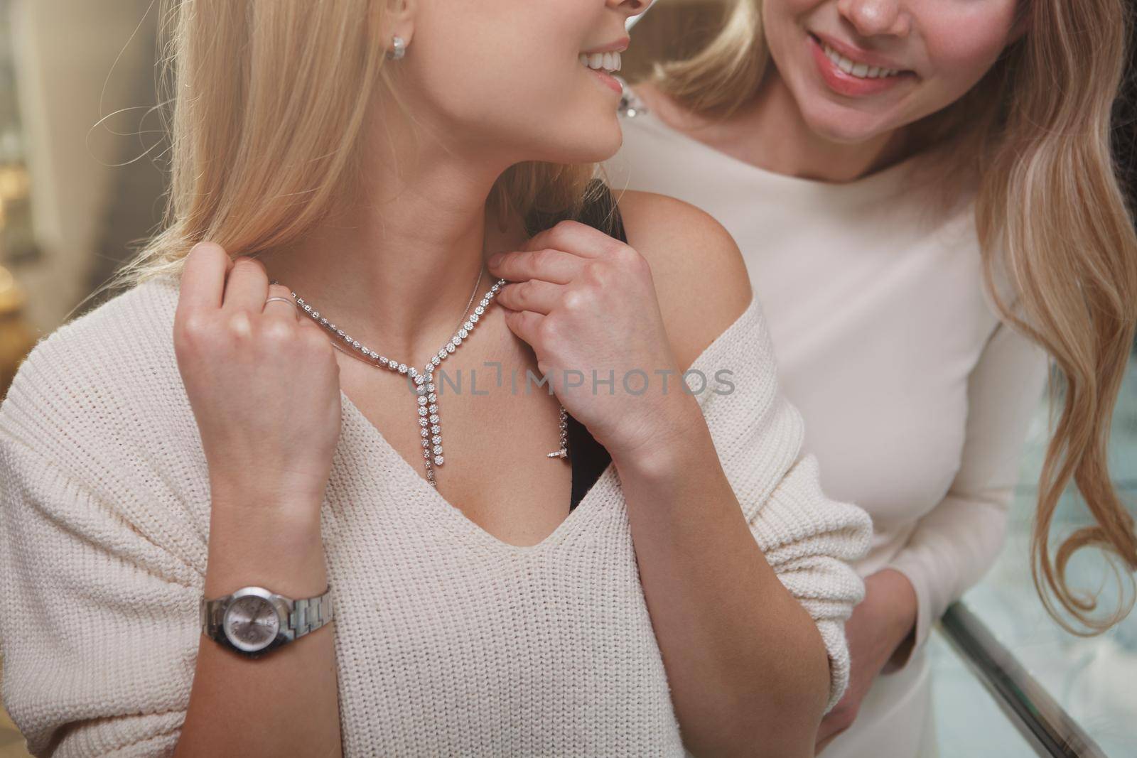 Cropped shot of woman smiling at her friend, trying on diamond necklace