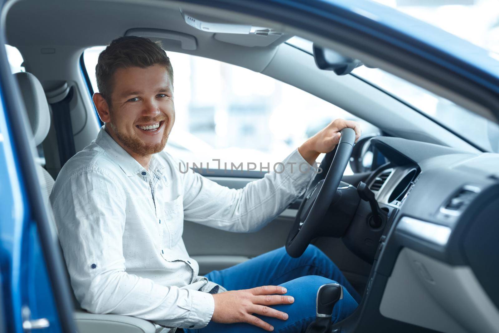 Dream came true. Portrait of a handsome bearded man sitting in his new car laughing to the camera happily