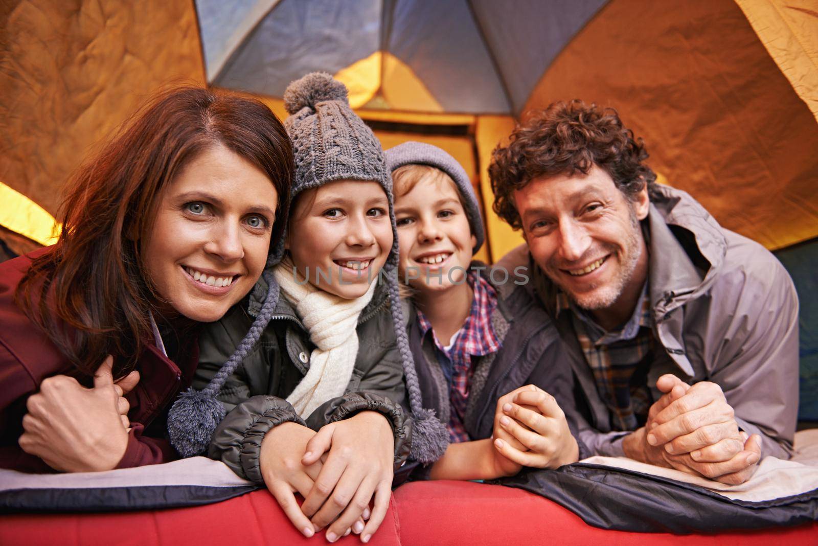 Family camping is family bonding. Portrait of smiling family of four relaxing in tent on a camping holiday