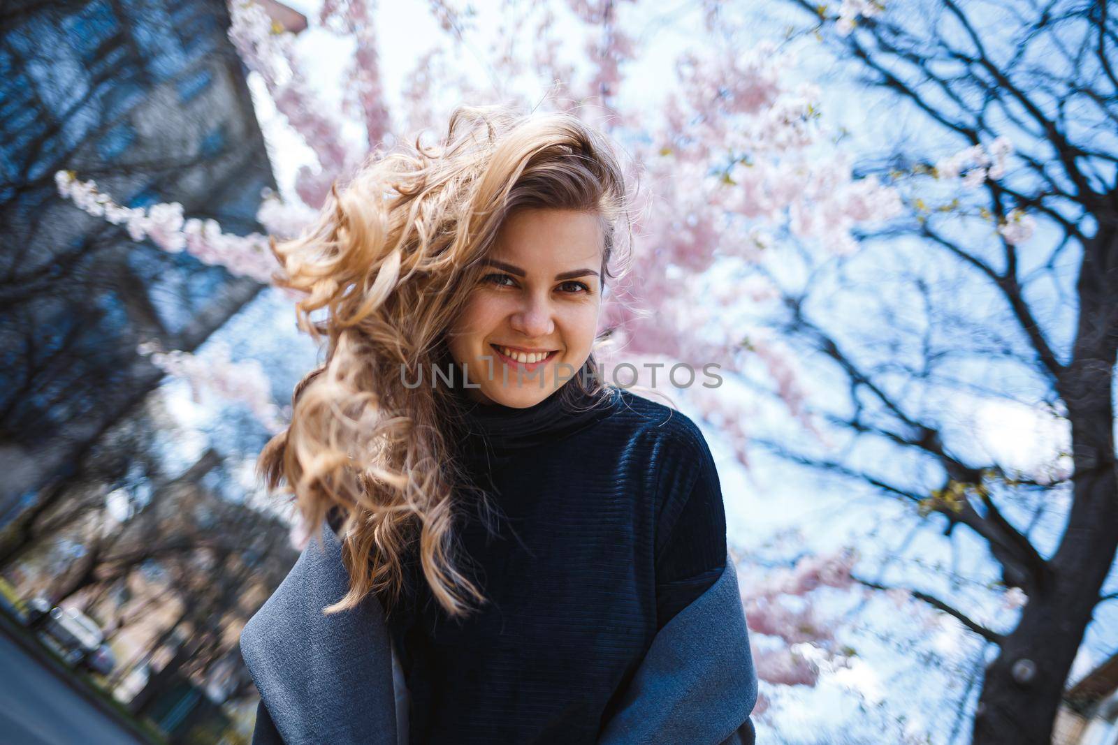 Sakura branches with flowers on a tree on the city streets. Happy woman girl spinning on the street with blooming sakura. Gorgeous fashionable girl outdoors. Sakura tree blossoms.