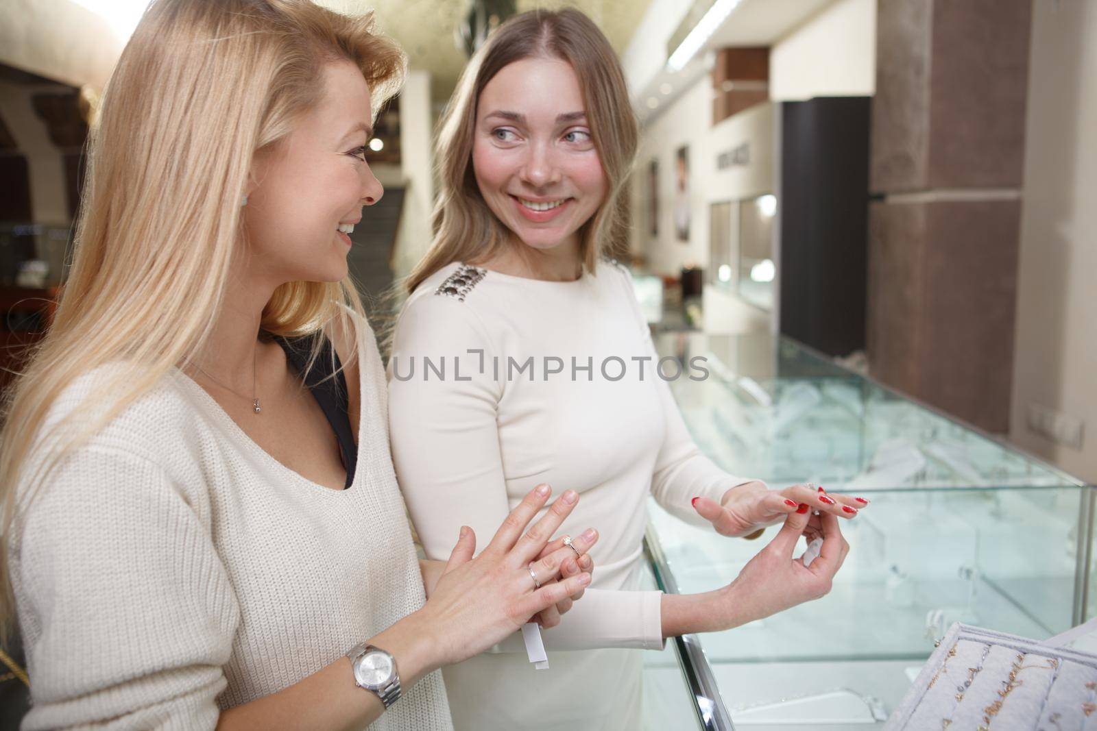 Cheerful woman talking to her friend while choosing jewelry to buy