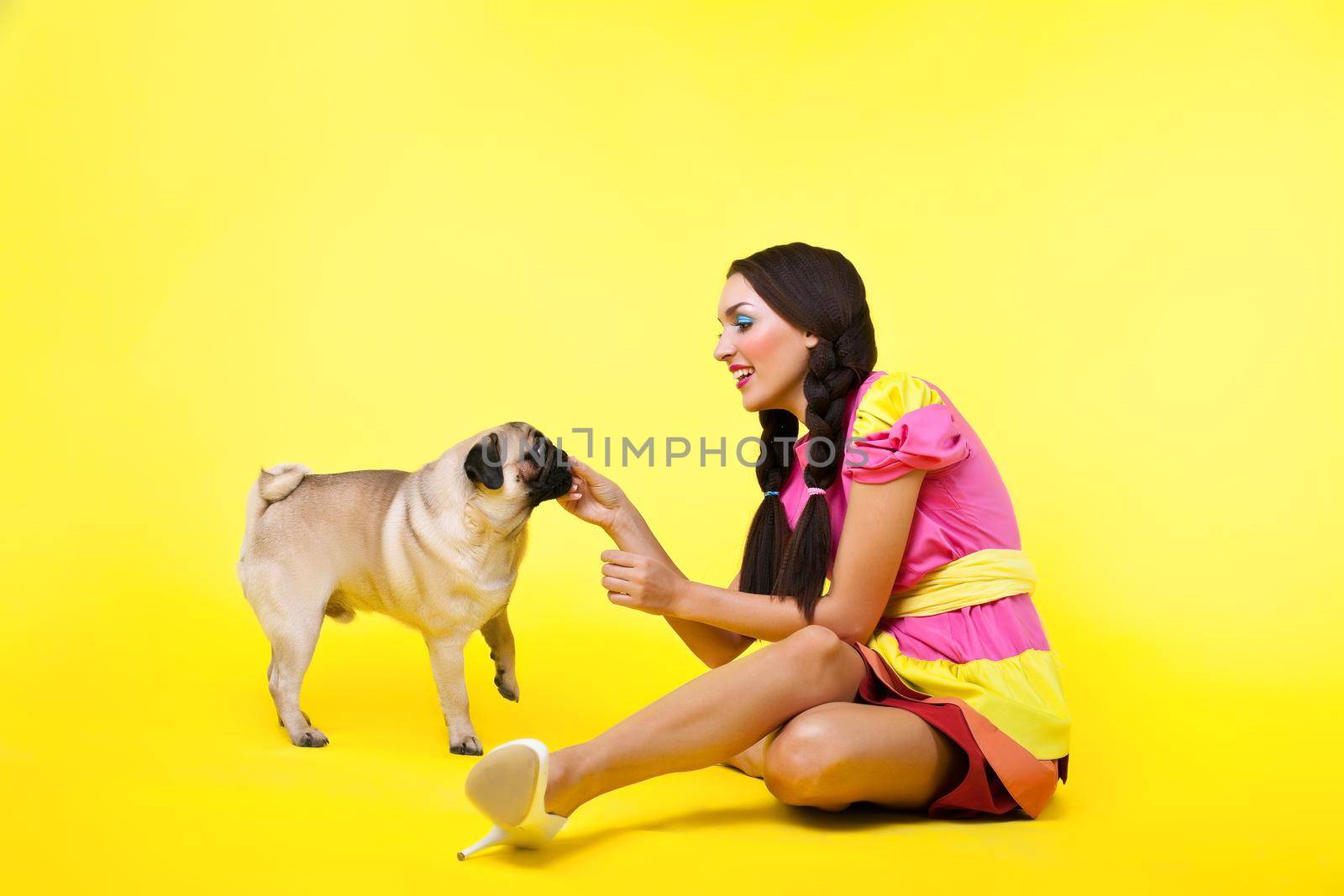 cute girl in doll dress feed a dog with cheese on yellow background