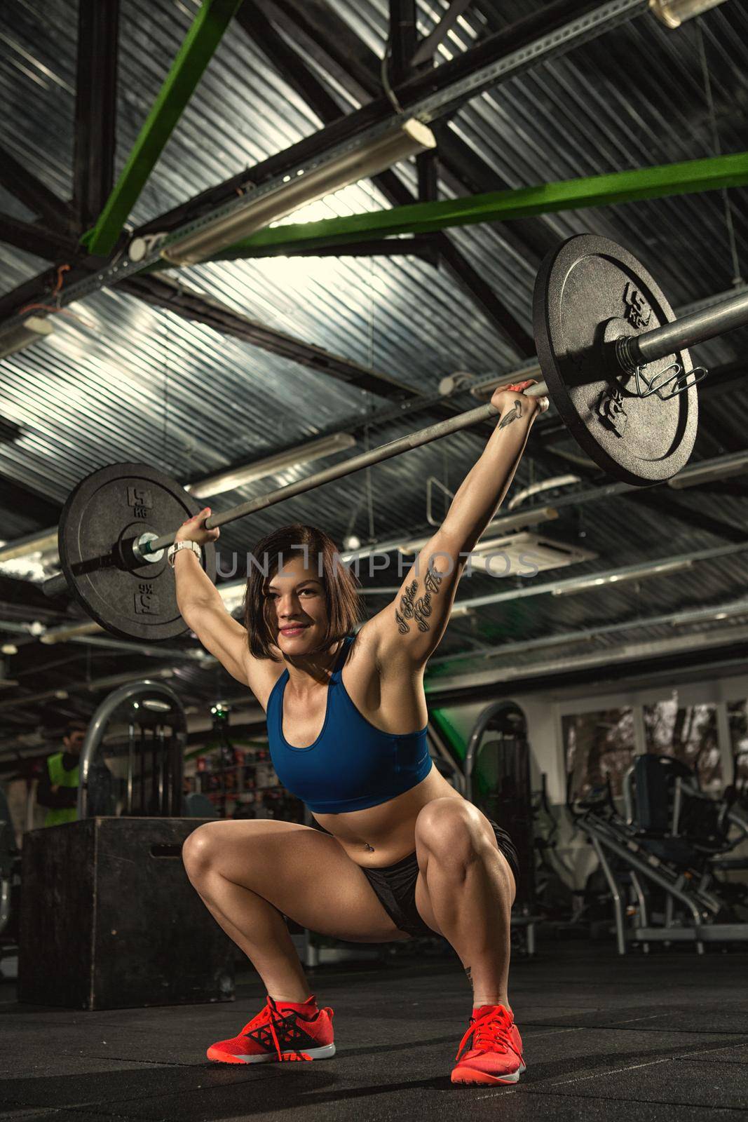 Active lifestyle. Vertical low angle shot of a beautiful young strong sportswoman smiling to the camera while doing squats with lifting barbell crossfit heavy duty functional cross training concept