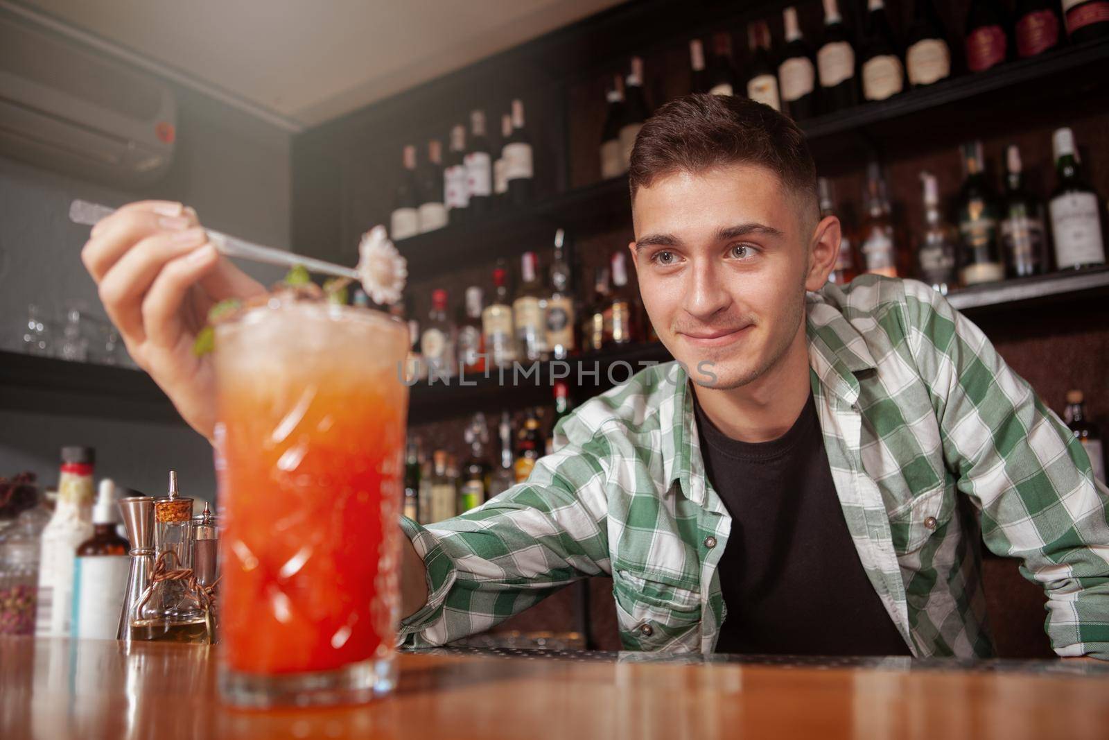 Handsome happy bartender enjoying working at the bar, garnishing cocktail for a client