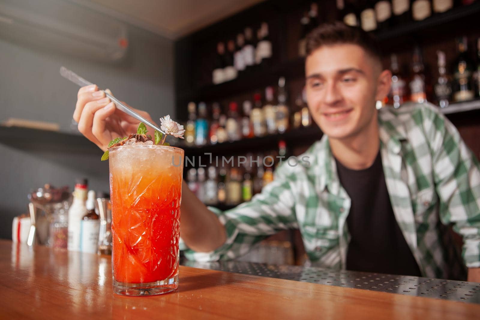 Selective focus on cocktail glass, cheerful bartender garnishing drink for a customer