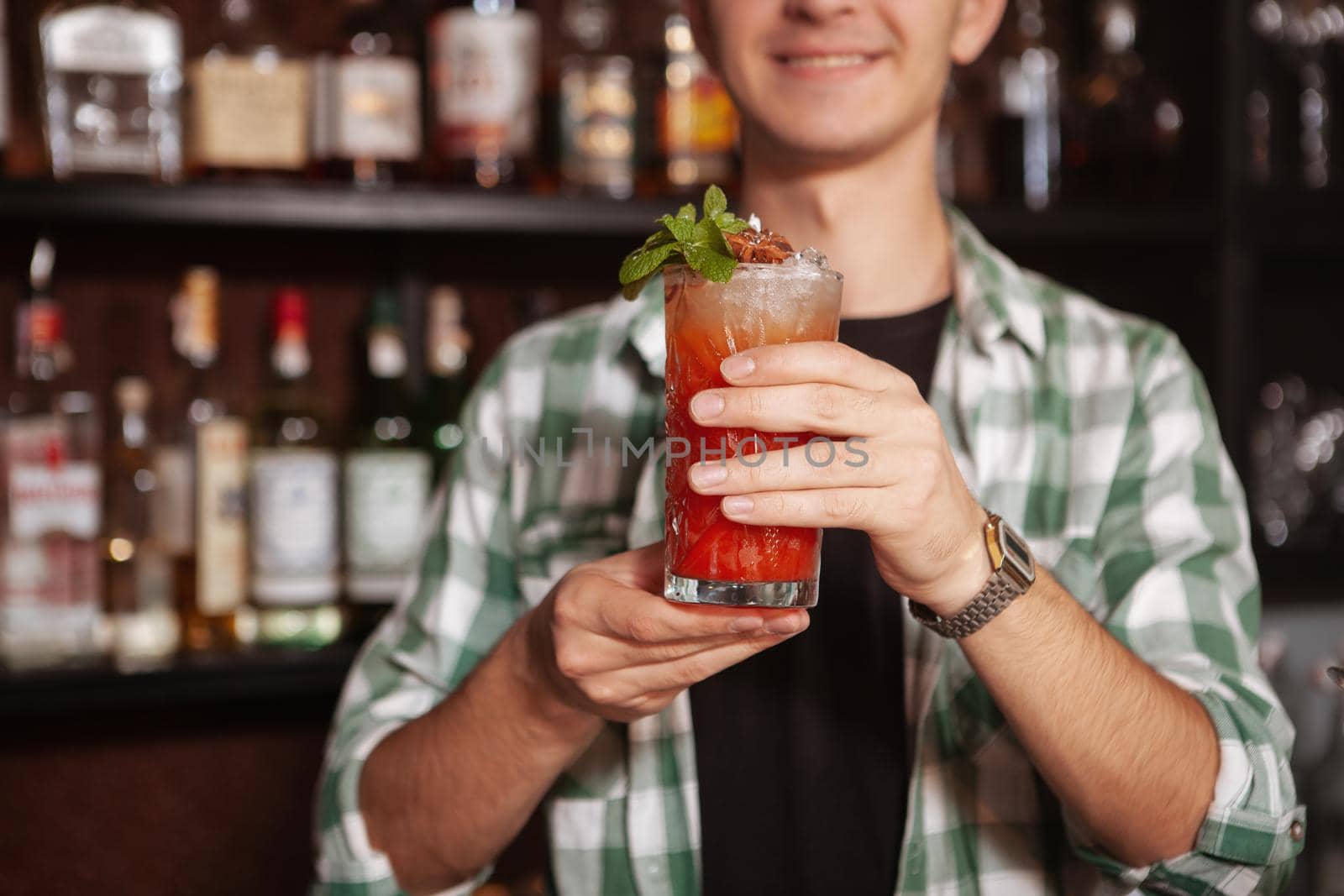 Cropped close up of a happy bartebder smiling, serving you delicious cocktail, copy space. Waiter holding a drink