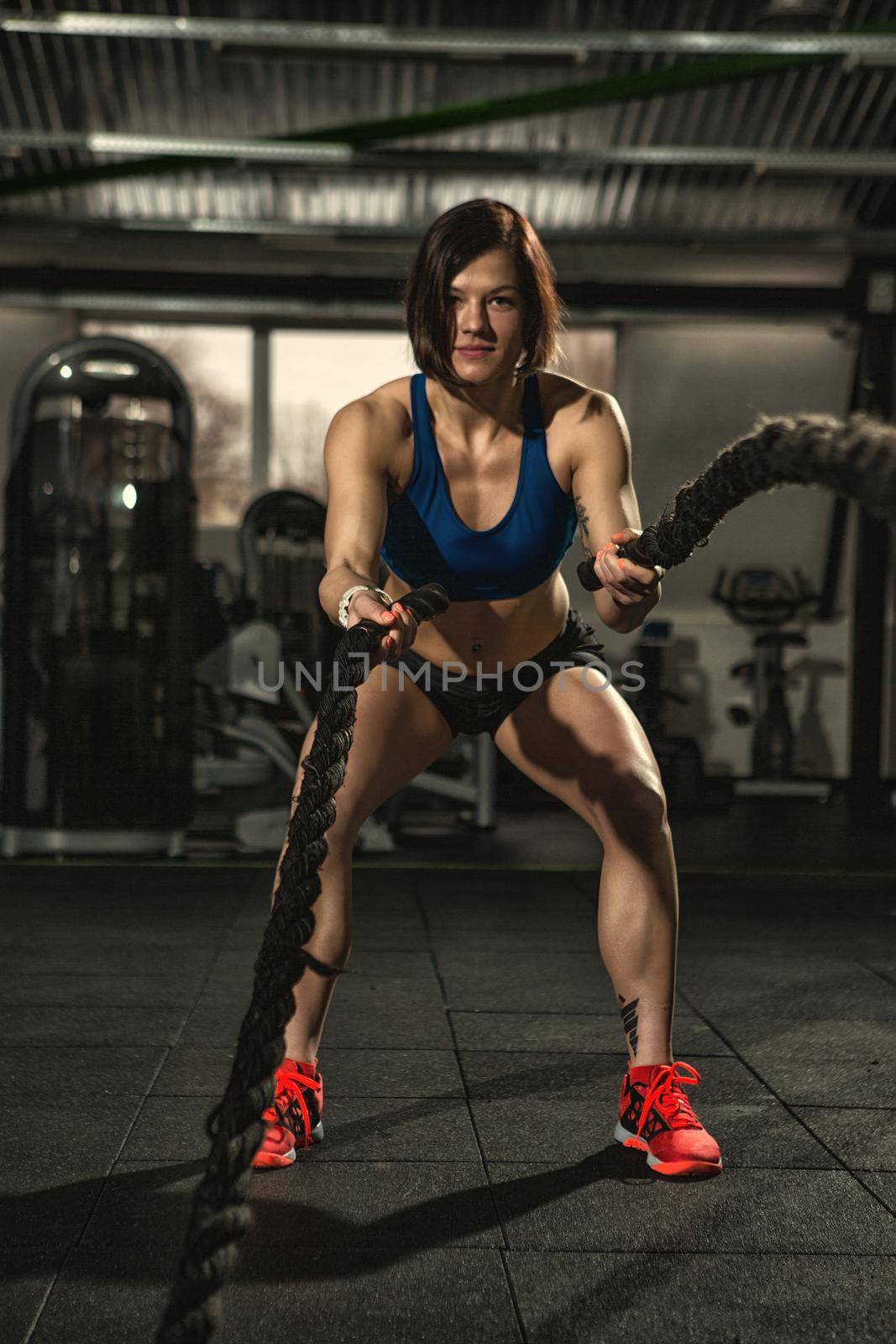 Crossfit workout. Vertical full length shot of an athletic fitness woman doing functional training exercise with battle ropes at the gym CrossFit cross training strength endurance energy power concept