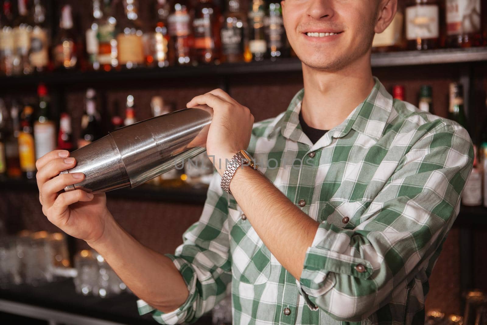 Close up cropped shot of unrecognizable male bartender preparing drink for a customer, using shaker tin