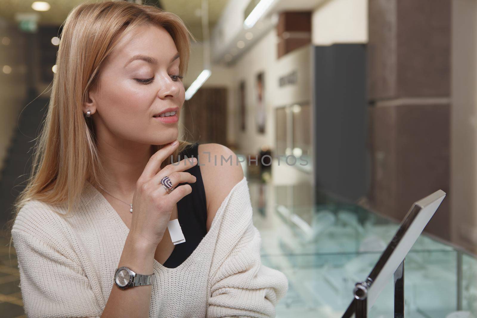 Attractive woman looking in the mirror at jewelry store, trying on jewellery