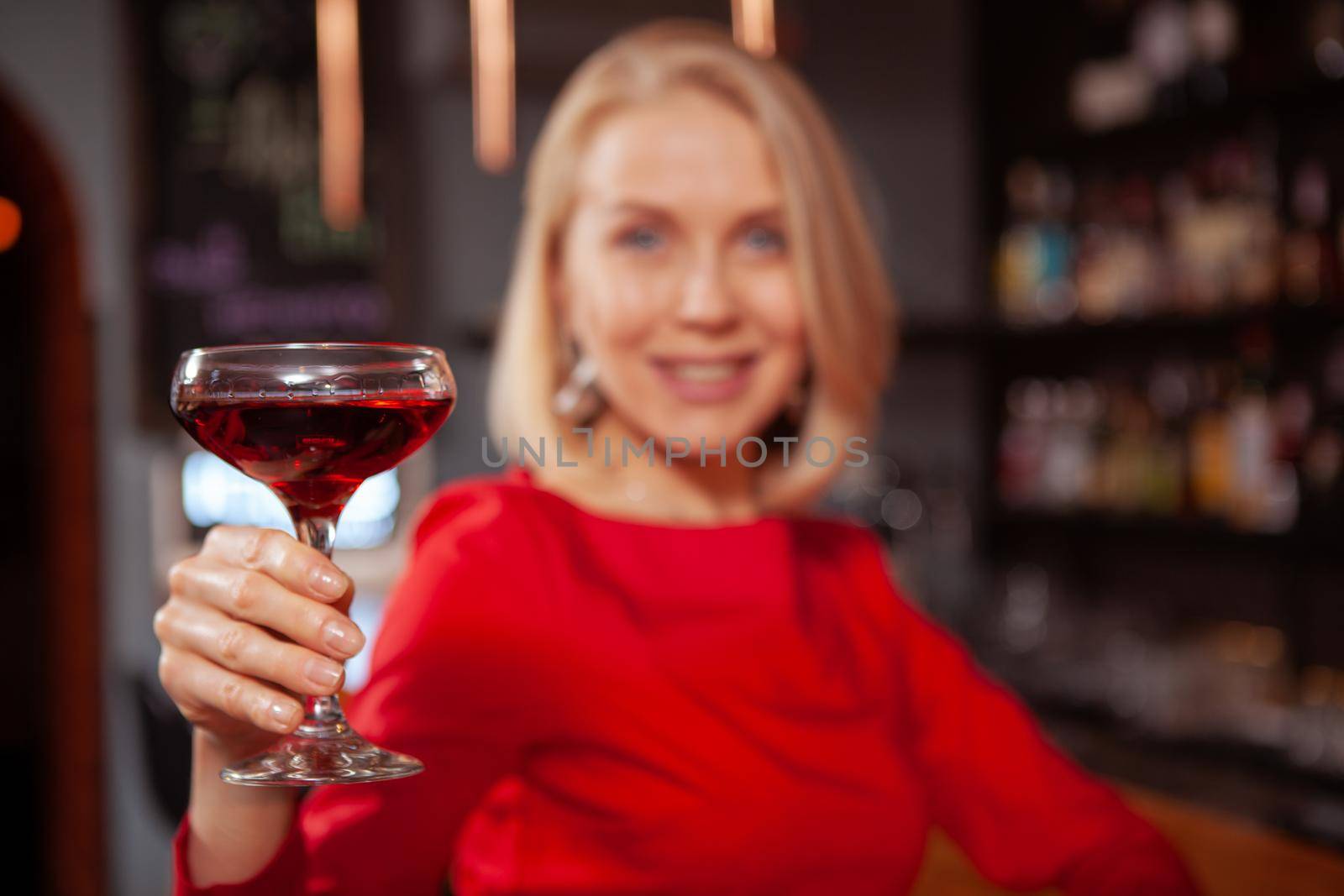 Close up of a cocktail happy elegant woman is holding out to the camera