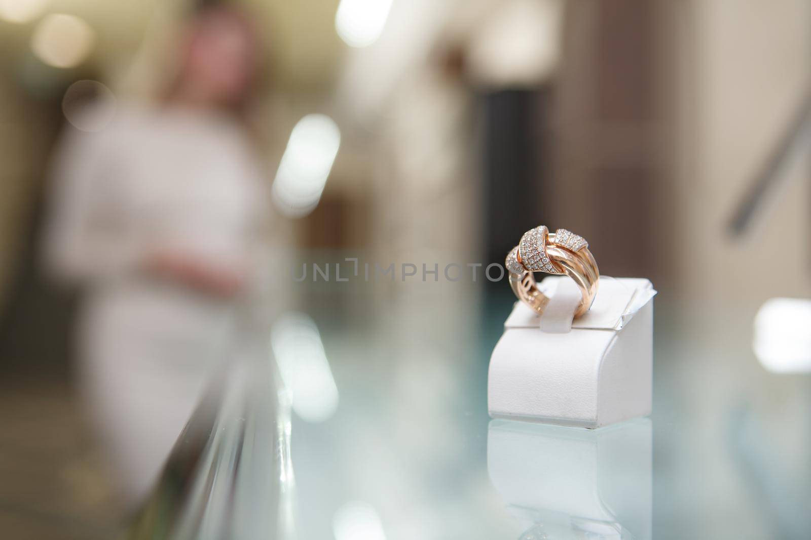 Close up of a golden ring with diamonds, woman shopping at jewelry store on background