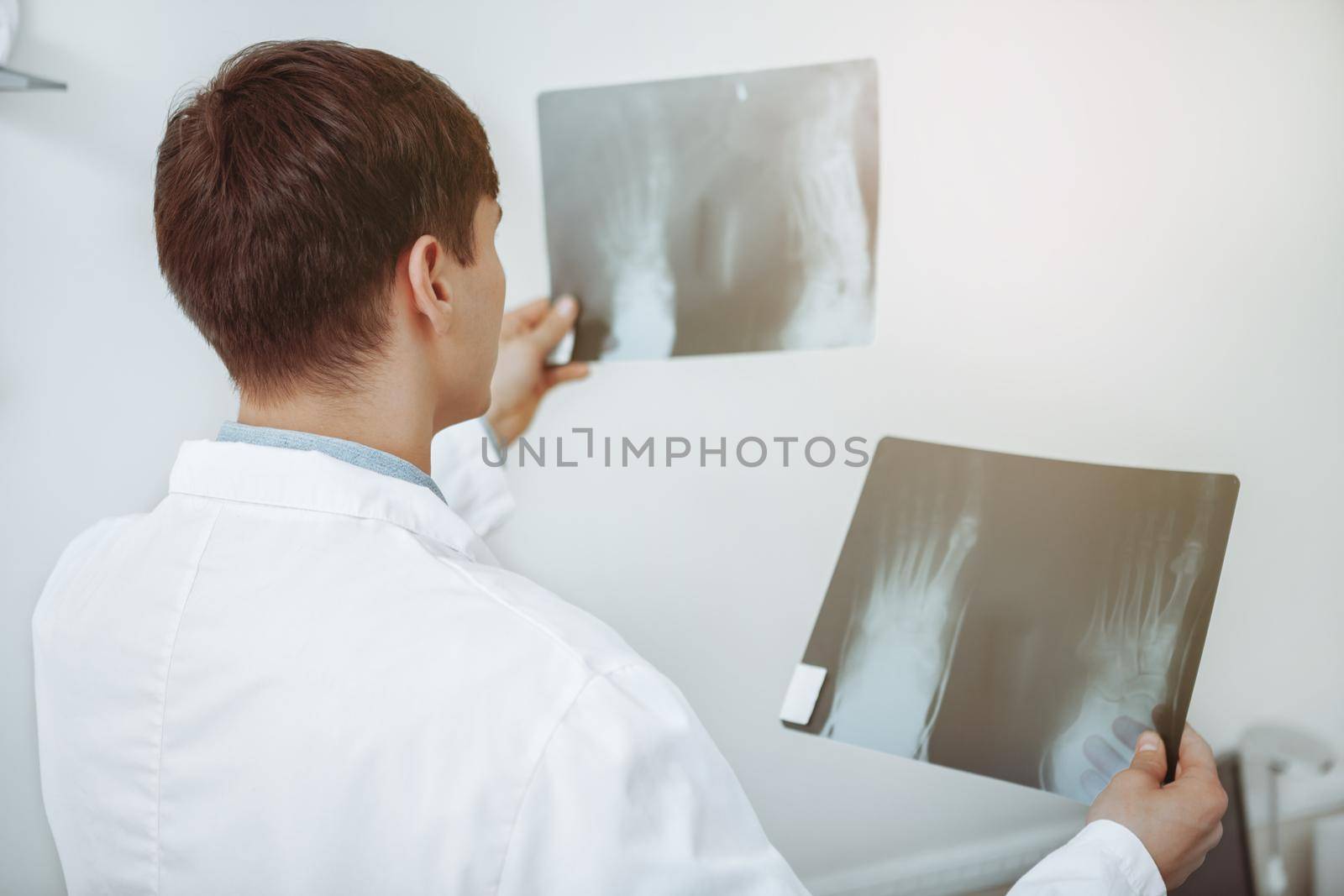 Rear view shot of an unrecognizable male doctor comparing two x-ray scans of a patient. Experienced doctor examining x-rays of his patient. Treatment, therapy, medicine concept