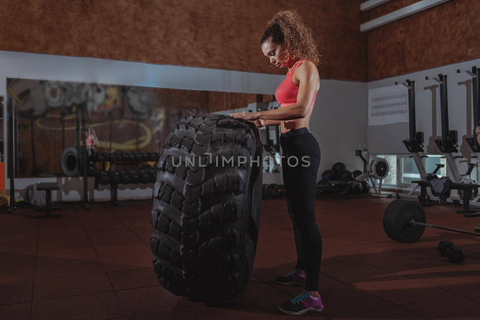 Full length of a beautiful athletic woman resting after flipping huge heavy tire, exercising at crossfit box gym. Attractive female crossfit athlete relaxing after training, copy space