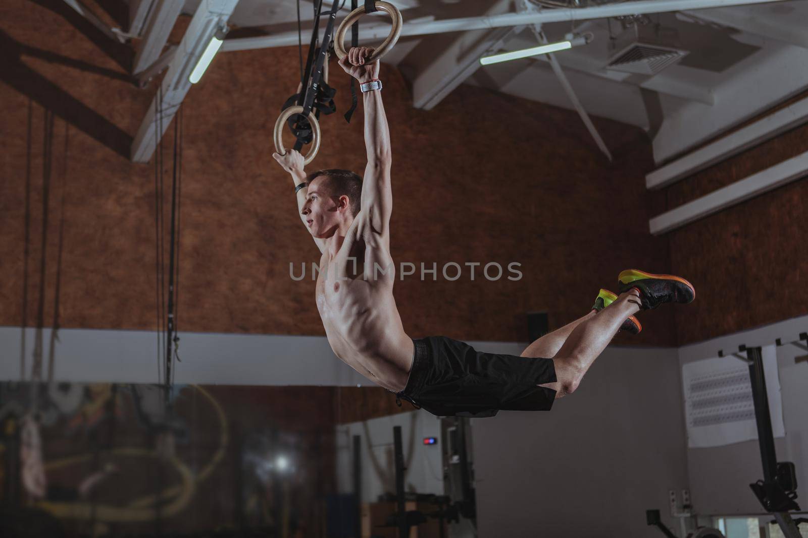 Young male crossfit athlete working out on gymnastic rings at the gym, copy space. Athletic man exercising on gymnastic rings at crossfit box gym