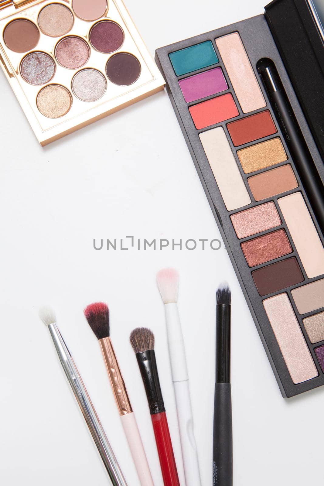 Vertical shot of eyeshadow palettes and makeup brushes isolated on white