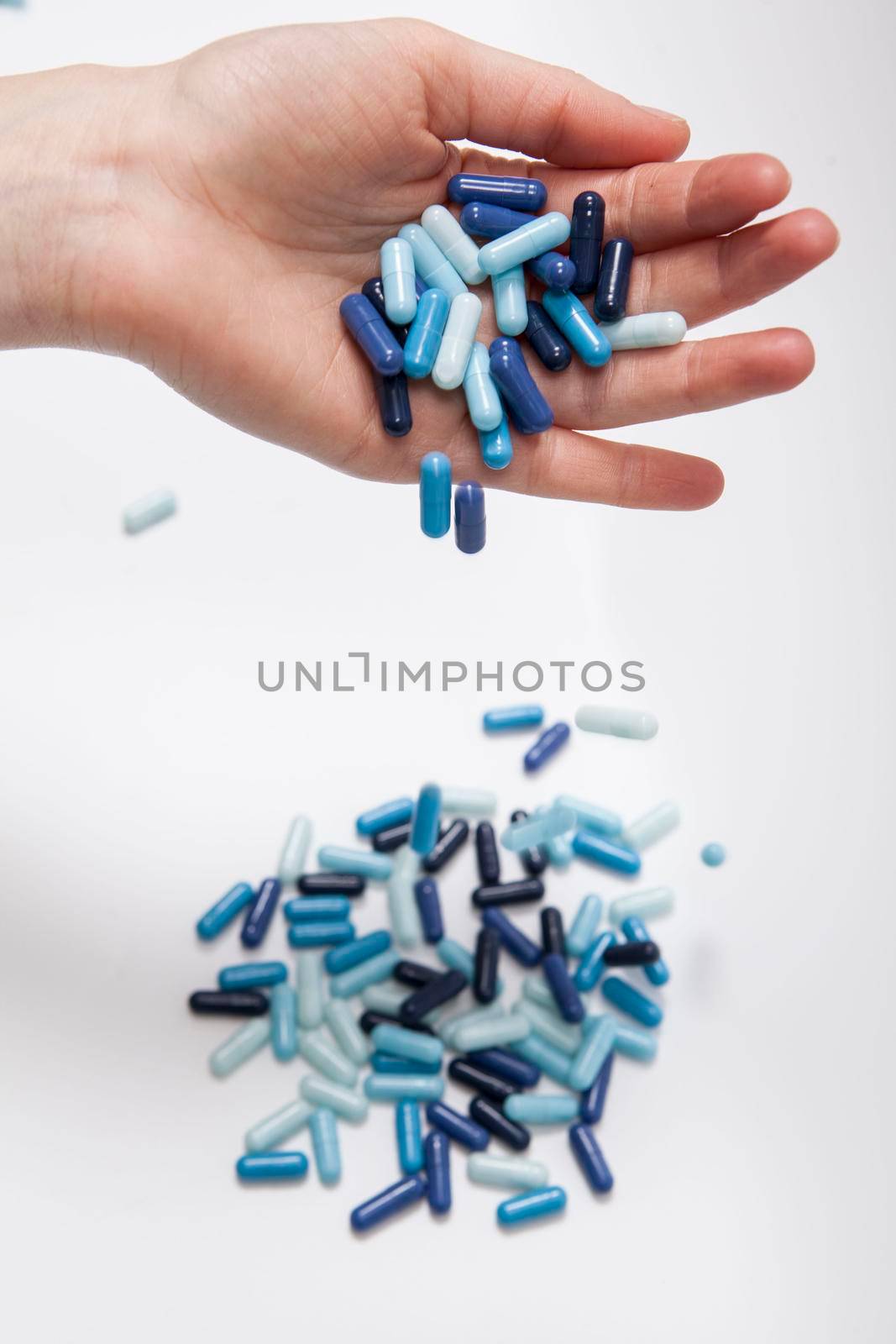 Vertical close up of medicament pills falling from the hand of unrecognizable person