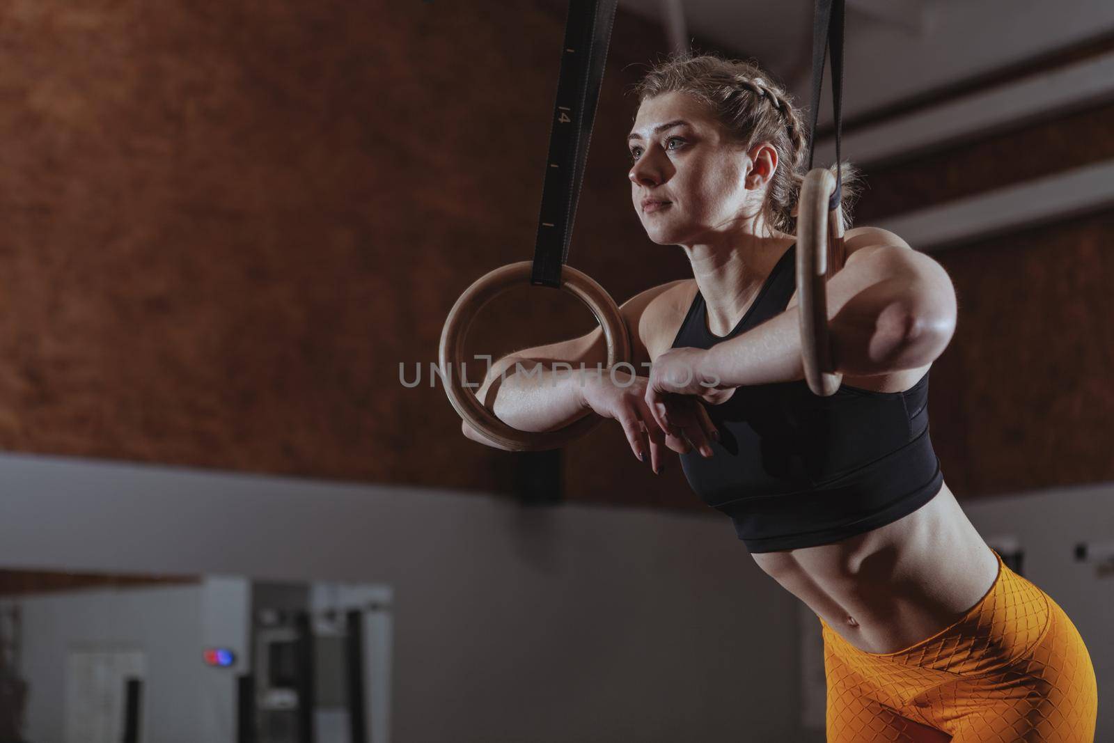 Low angle shot of a young athletic woman looking away thoughtfully, resting after working out on gymnastc rings. Female crossfit athlete relaxing after exercising, copy space
