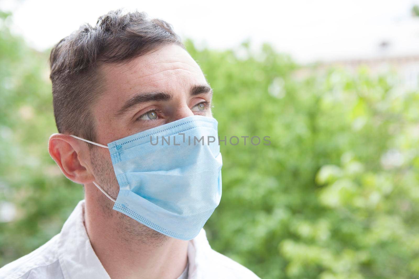 Close up portrait of a man looking away thoughtfully, wearing medical protective mask outdoors in the park