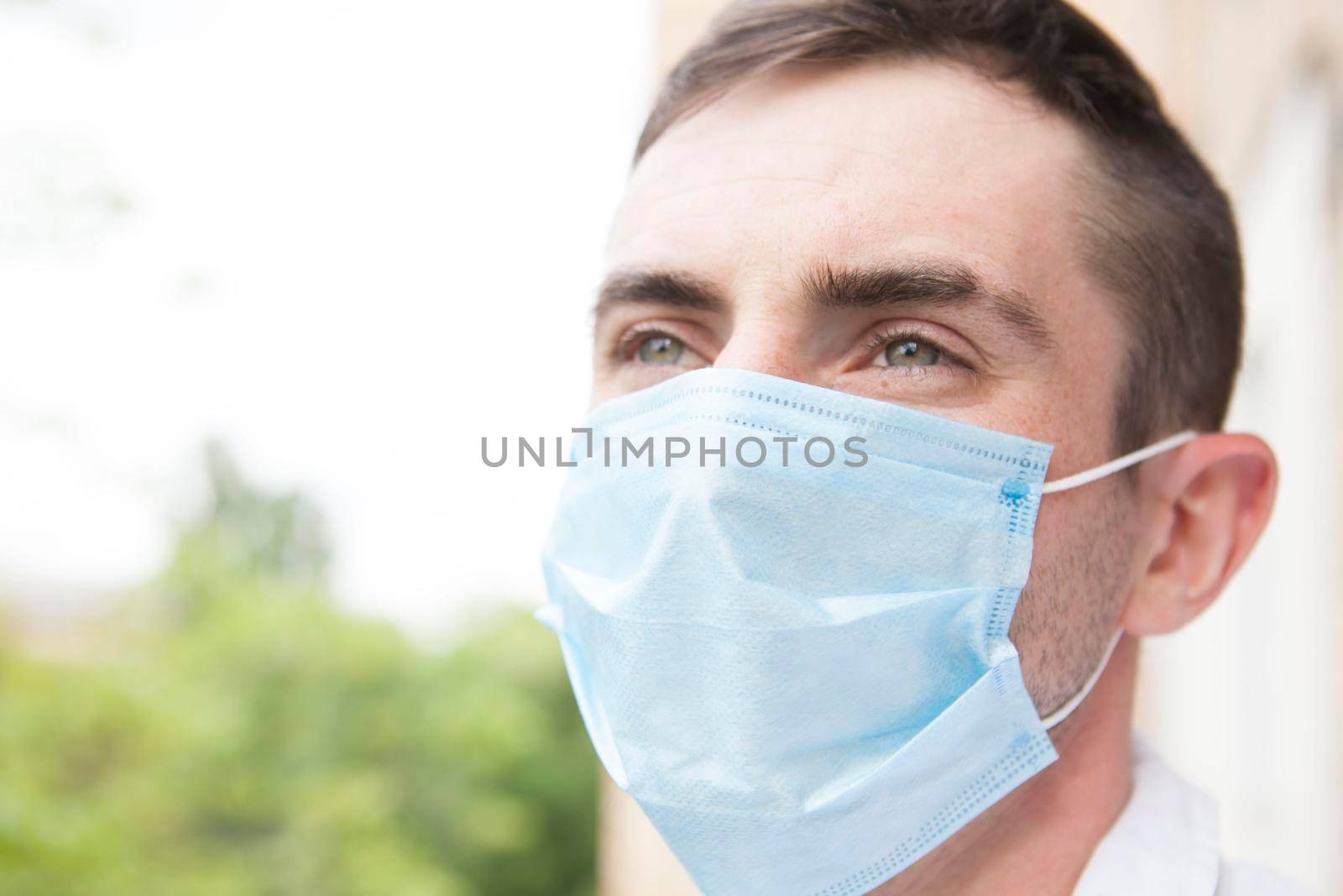 Happy young man looking away thoughtfully, wearing protective medical mask outdoors