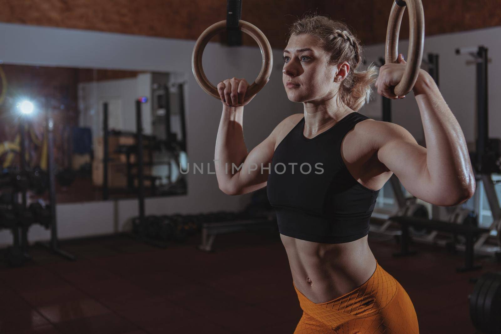 Low angle shot of young muscular female crossfit athlete resting on gymnastic rings, copy space. Charming sportswoman with fit toned strong body preparing to workout on gymnastic rings