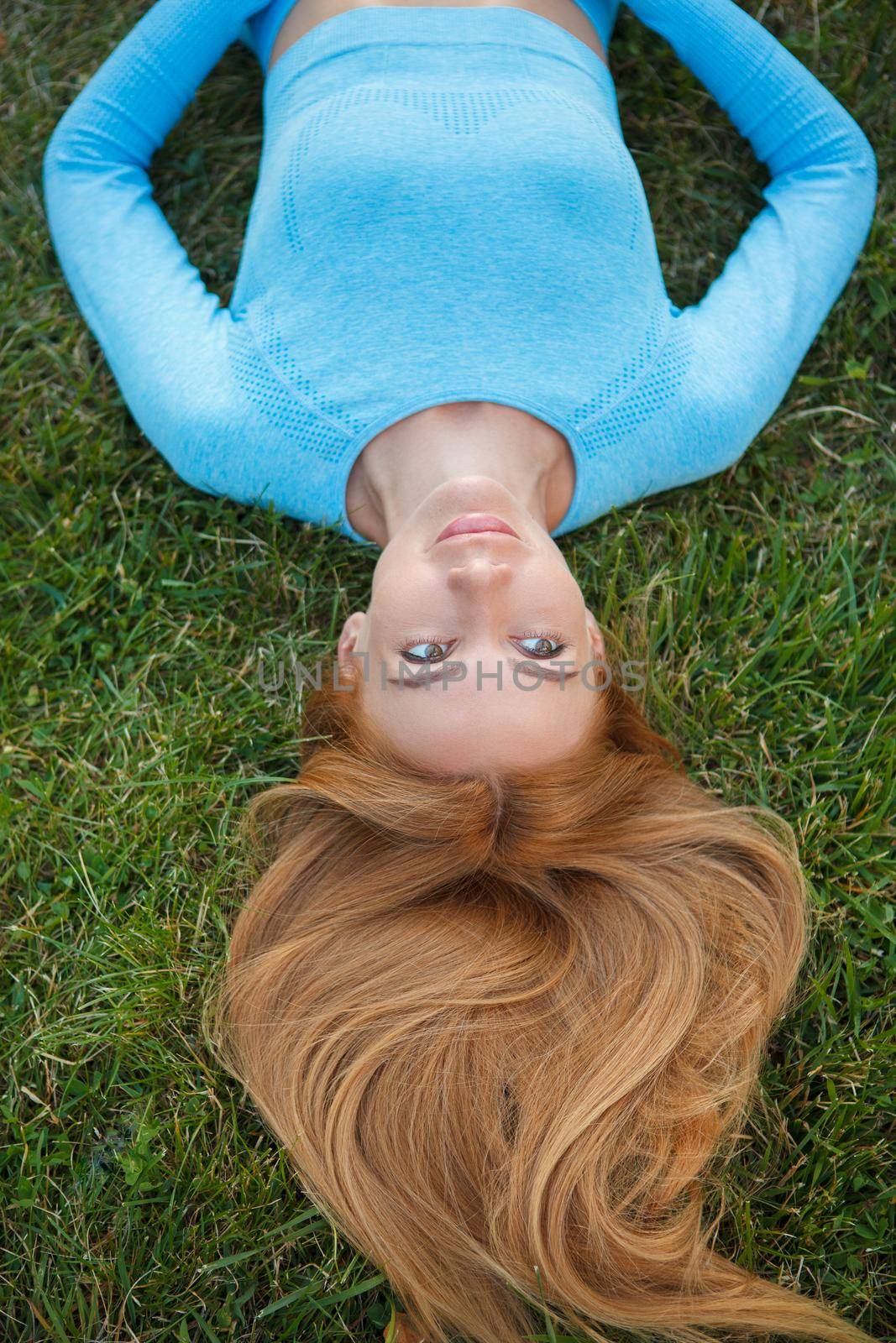 Vertical top view shot of a happy beautiful woman smiling, lying on green grass