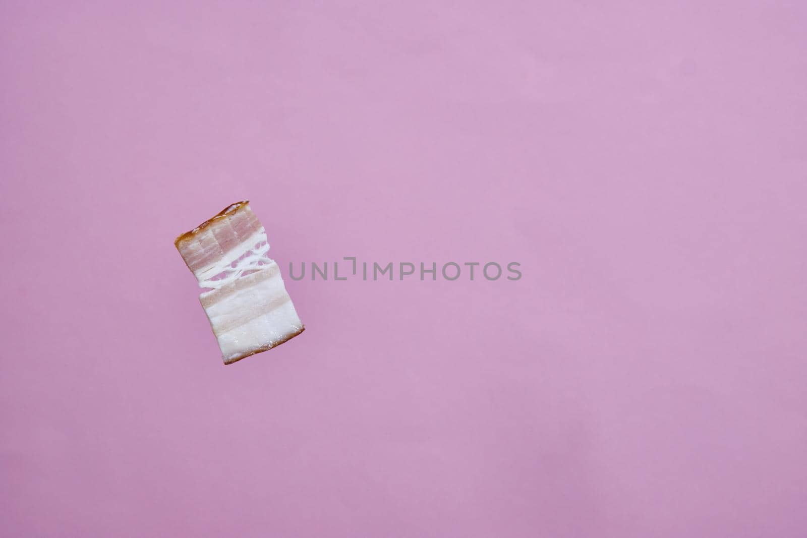 a piece of smoked salted bacon on a pink background.