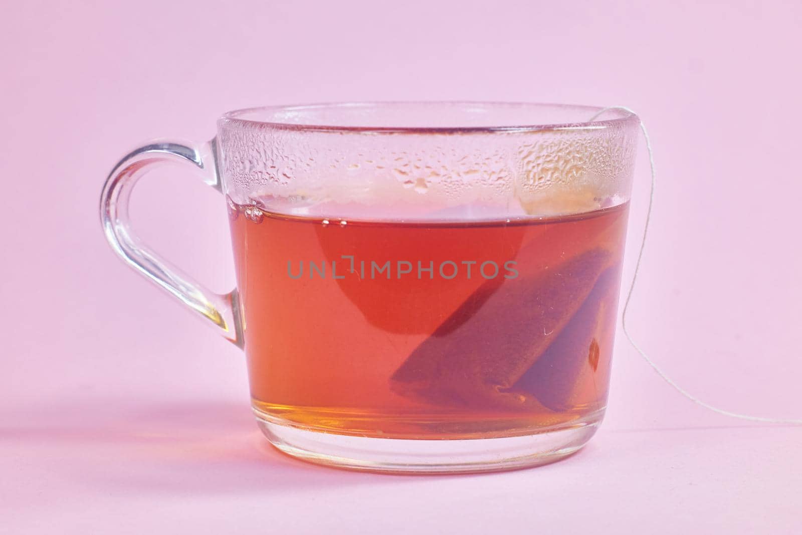 the tea bag is brewed in a transparent glass cup on a pink background.