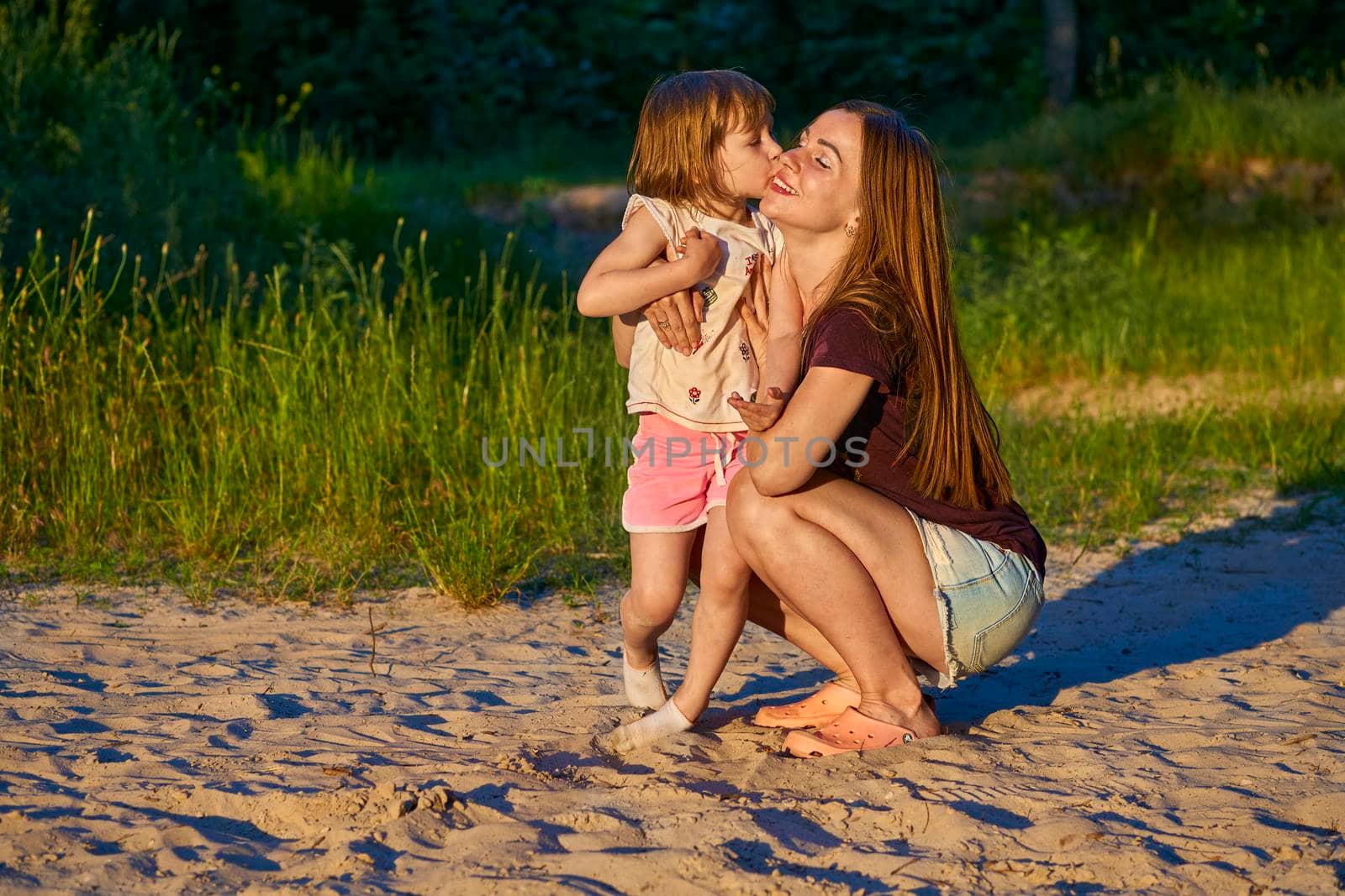 Wonderful cute girl child kissing happy mom among sand dunes and greenery by jovani68