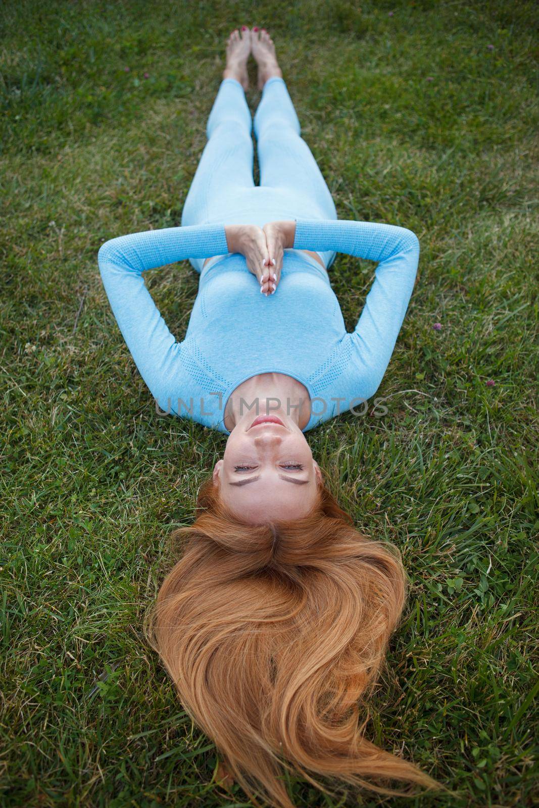 Vertical full length shot of a happy healthy athletic woman lying on the grass in shavasana, relaxing after outdoor workout