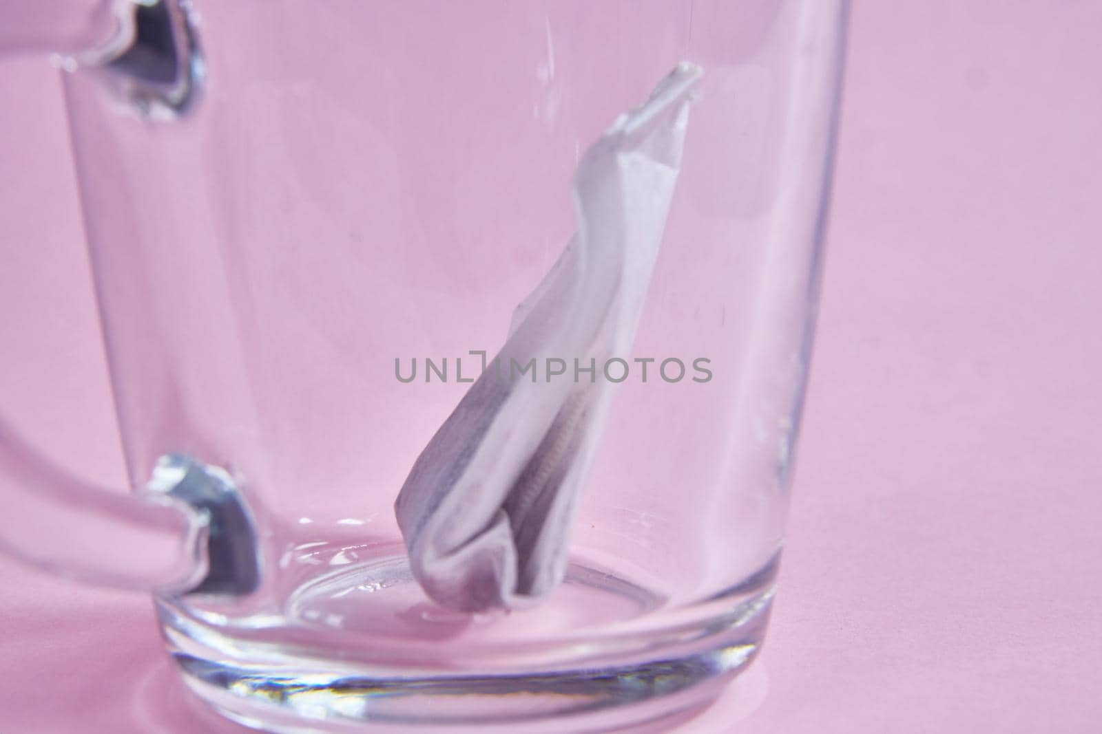 tea bag in an empty transparent glass cup on a pink background.