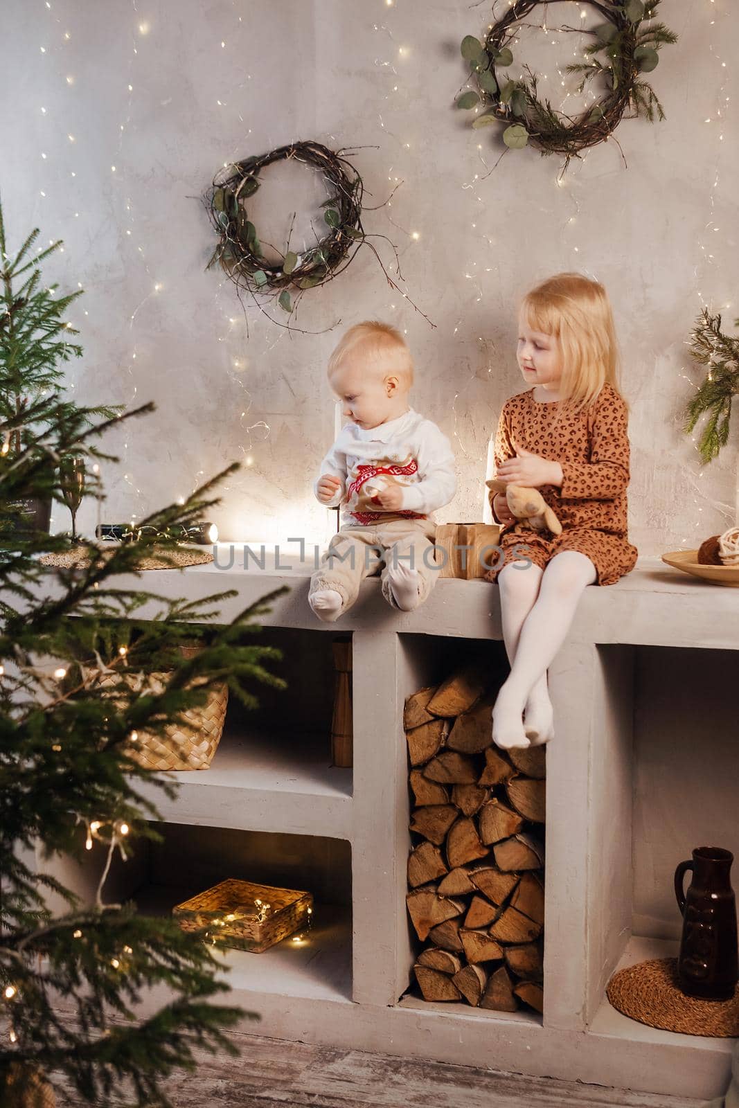 Little brother and sister play on Christmas eve in a beautiful house decorated for the New Year holidays. Children are playing with a Christmas gift. Scandinavian-style interior with live fir trees and a wooden staircase.