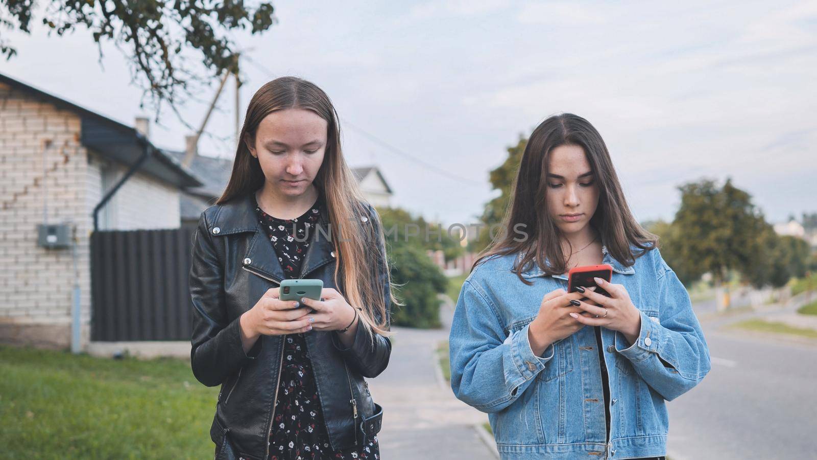 Two girlfriends watch a smartphone and walk through the village