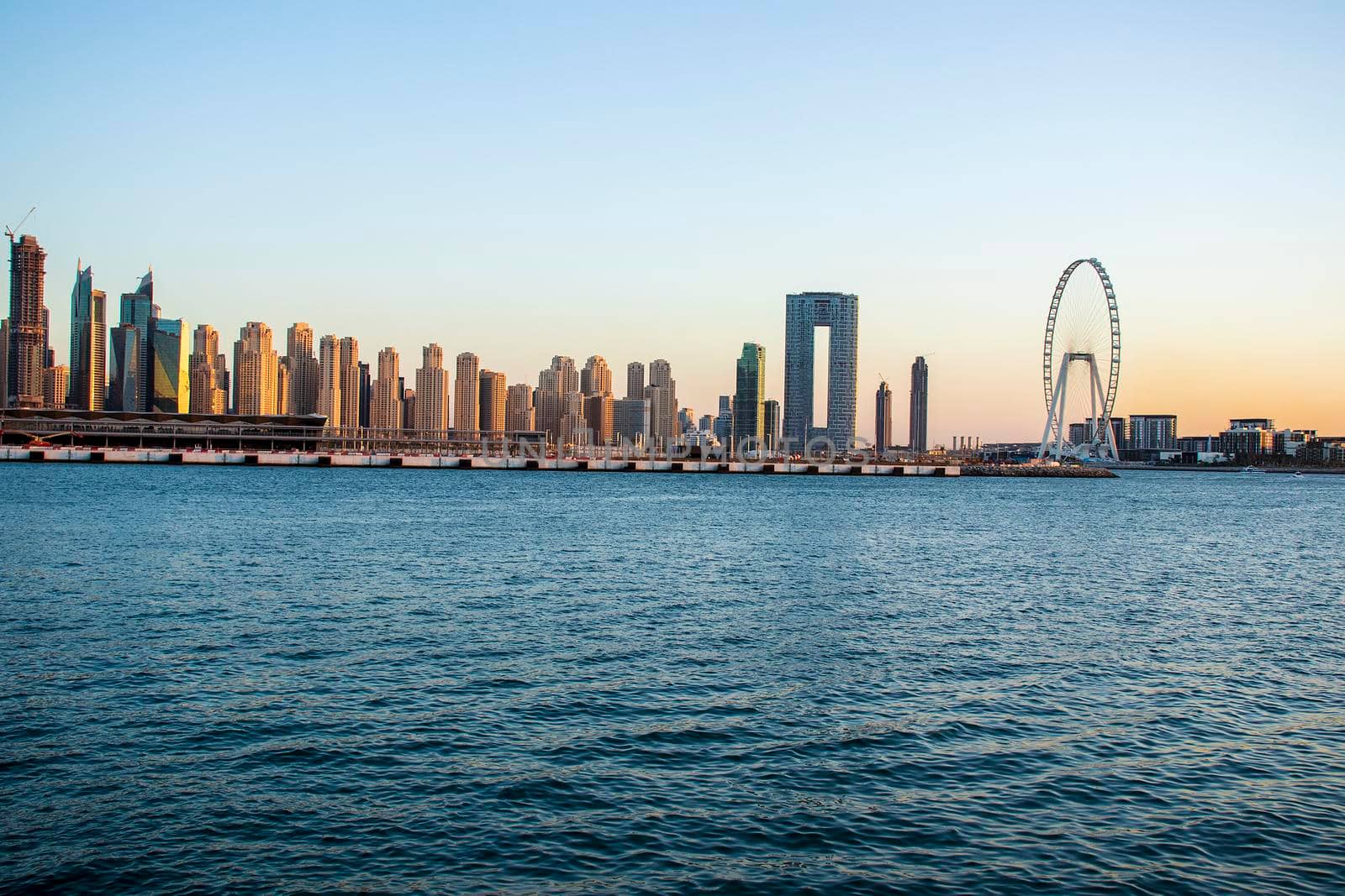 View of A Jumeirah Beach Residence and Blue waters during sunset hour. Shot made from Palm Jumeirah, man made island. Tallest ferris wheel, Ain Dubai can also be seen in the scene Dubai, UAE. by pazemin