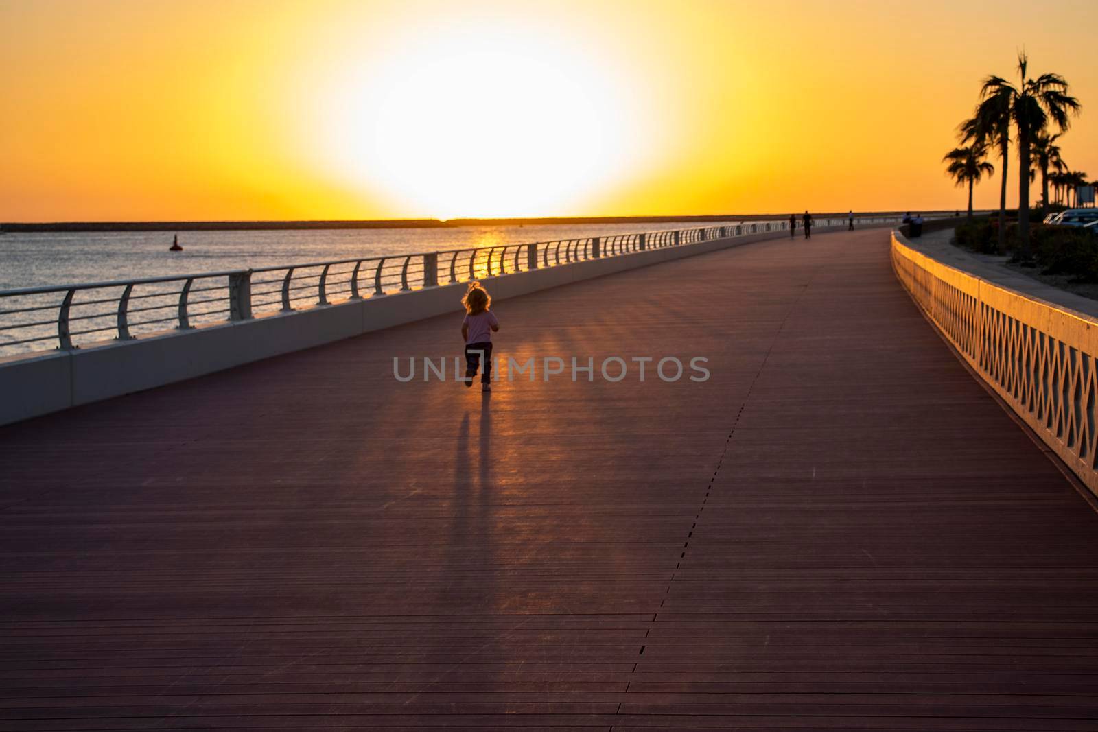 Little girl running on the boardwalk during sunset hour. Outdoors.