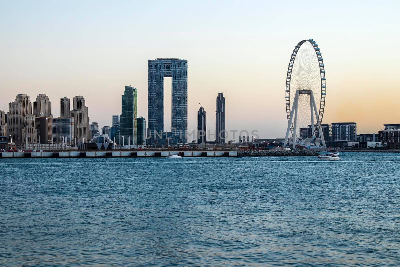 View of A Jumeirah Beach Residence and Blue waters during sunset hour. Shot made from Palm Jumeirah, man made island. Tallest ferris wheel, Ain Dubai can also be seen in the scene Dubai, UAE. Outdoors.