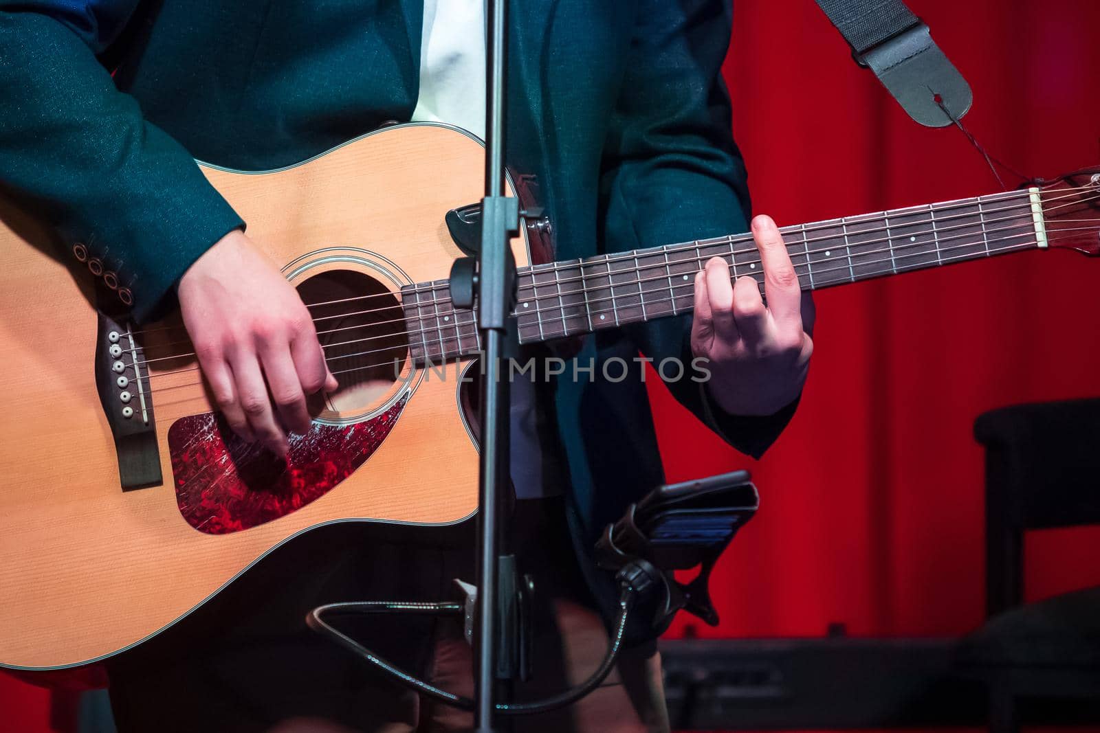 Man plays classical guitar against red curtain