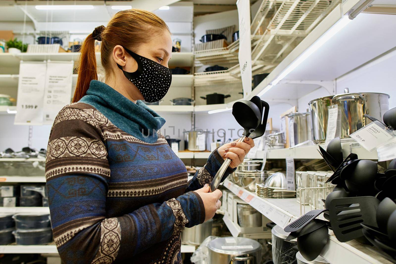 a woman in a protective mask chooses dishes and kitchen accessories in a supermarket, life with protection from infection in the new realities.