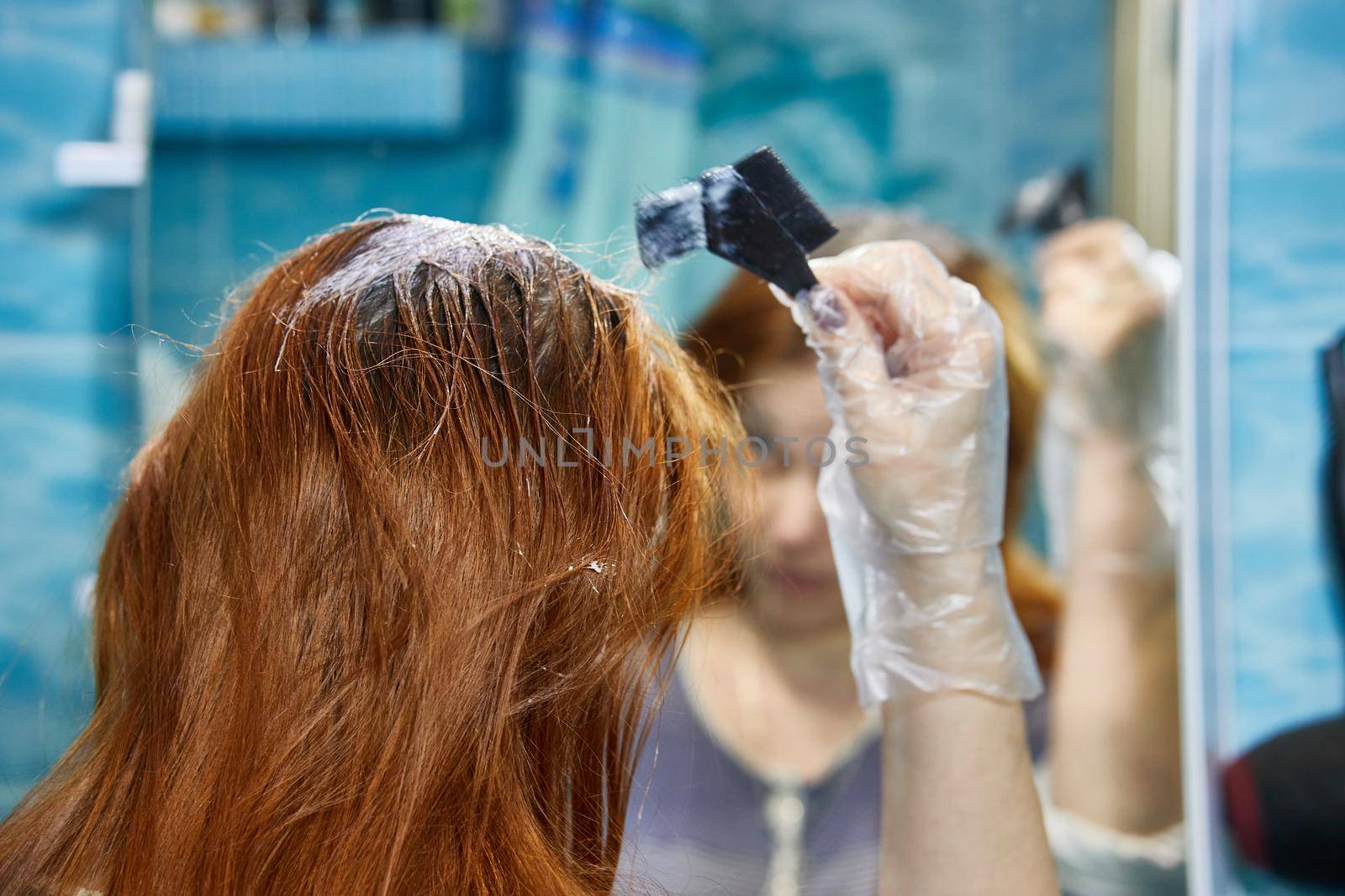 a woman dyes her hair red, coloring the hair roots with henna or dye.