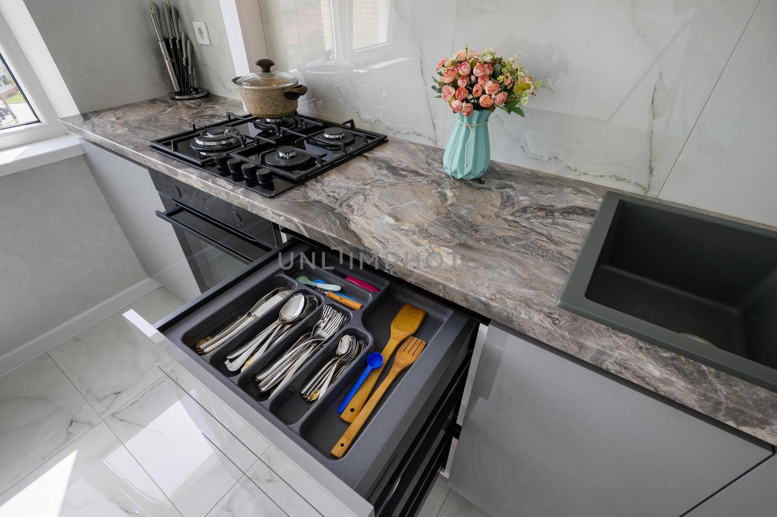 High angle closeup view to retracted drawer of grey and white modern domestic kitchen with kitchen utensils such as forks, spoons, knives