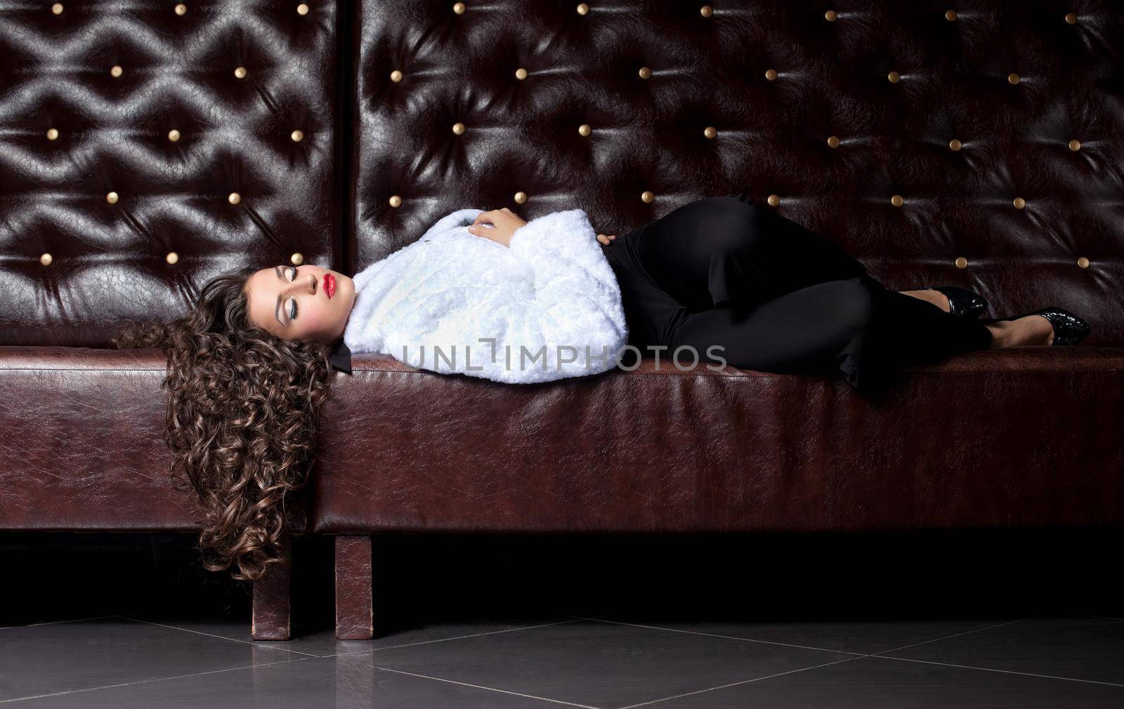 sexy young woman lay on leather sofa in fur coat