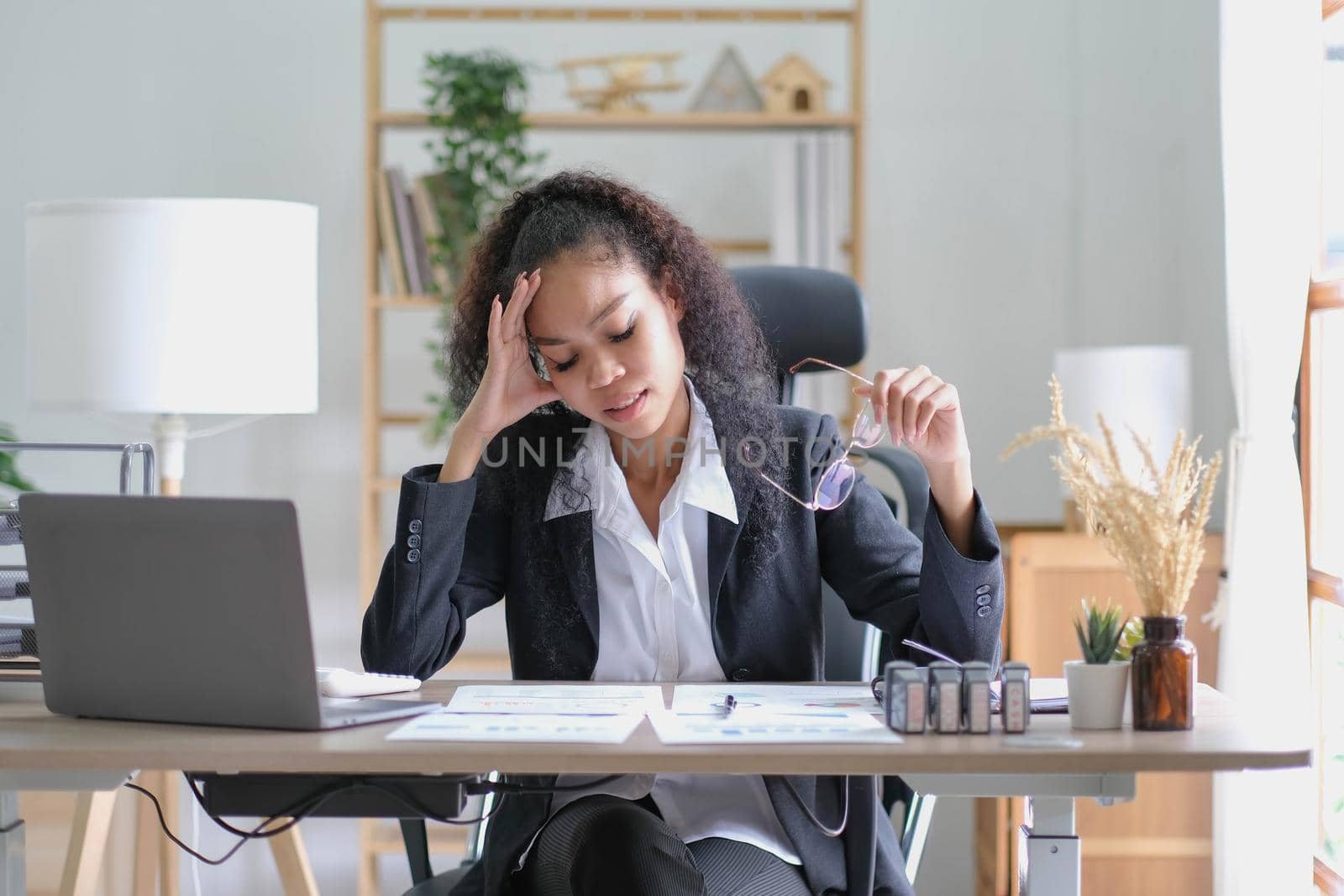 Serious african american businesswoman sitting at table looking at laptop screen. Ethnic woman read message email with important news, business documents online, chatting with clients working remotely by wichayada