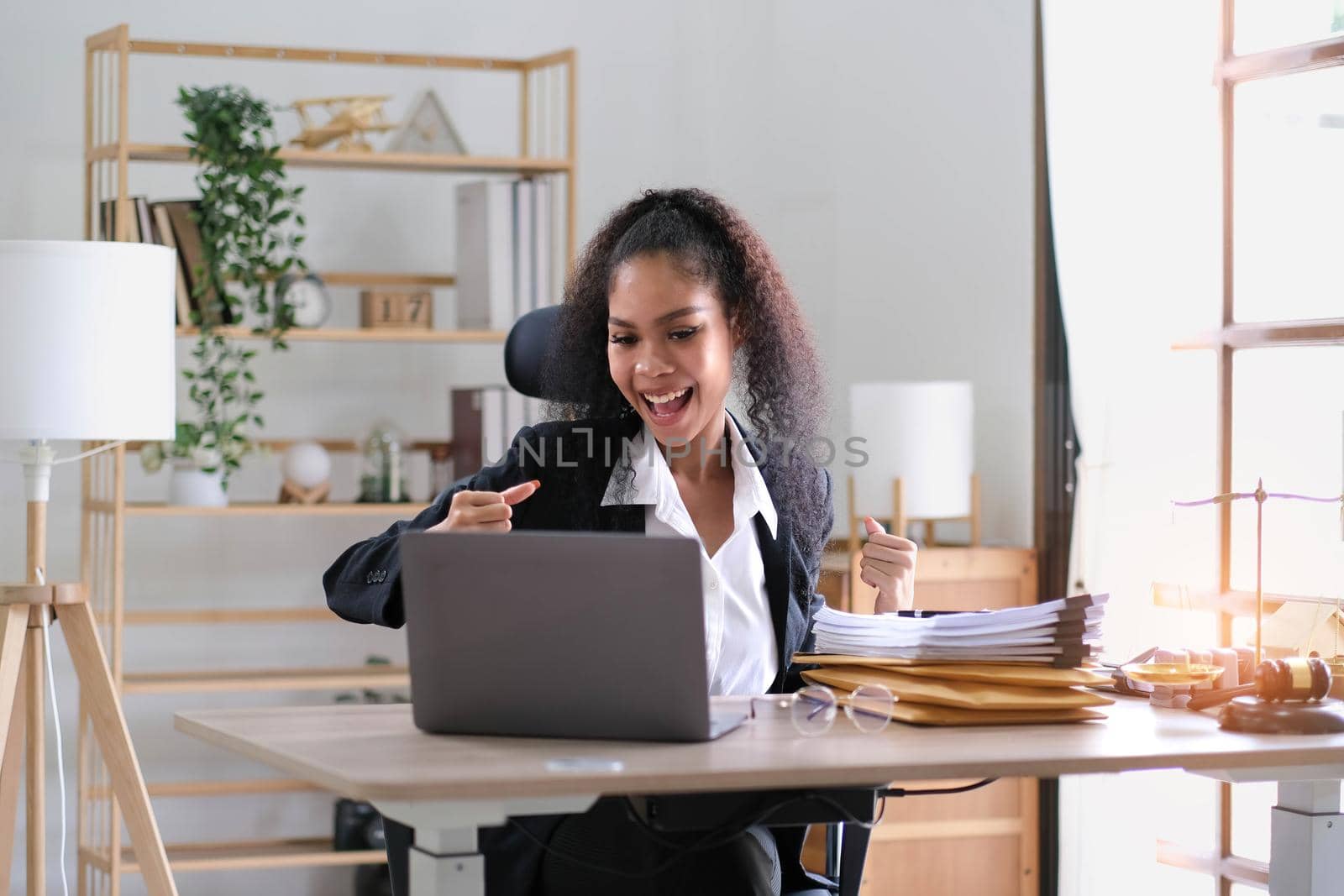 Young success american businesswoman raising her hands up and laughing with happiness at office.