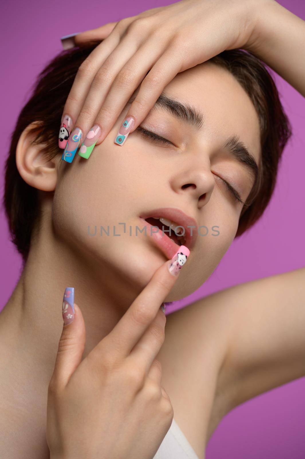 Sensual studio portrait of young pretty girl with short haircut and extravagant nail art, eyes closed, colored background