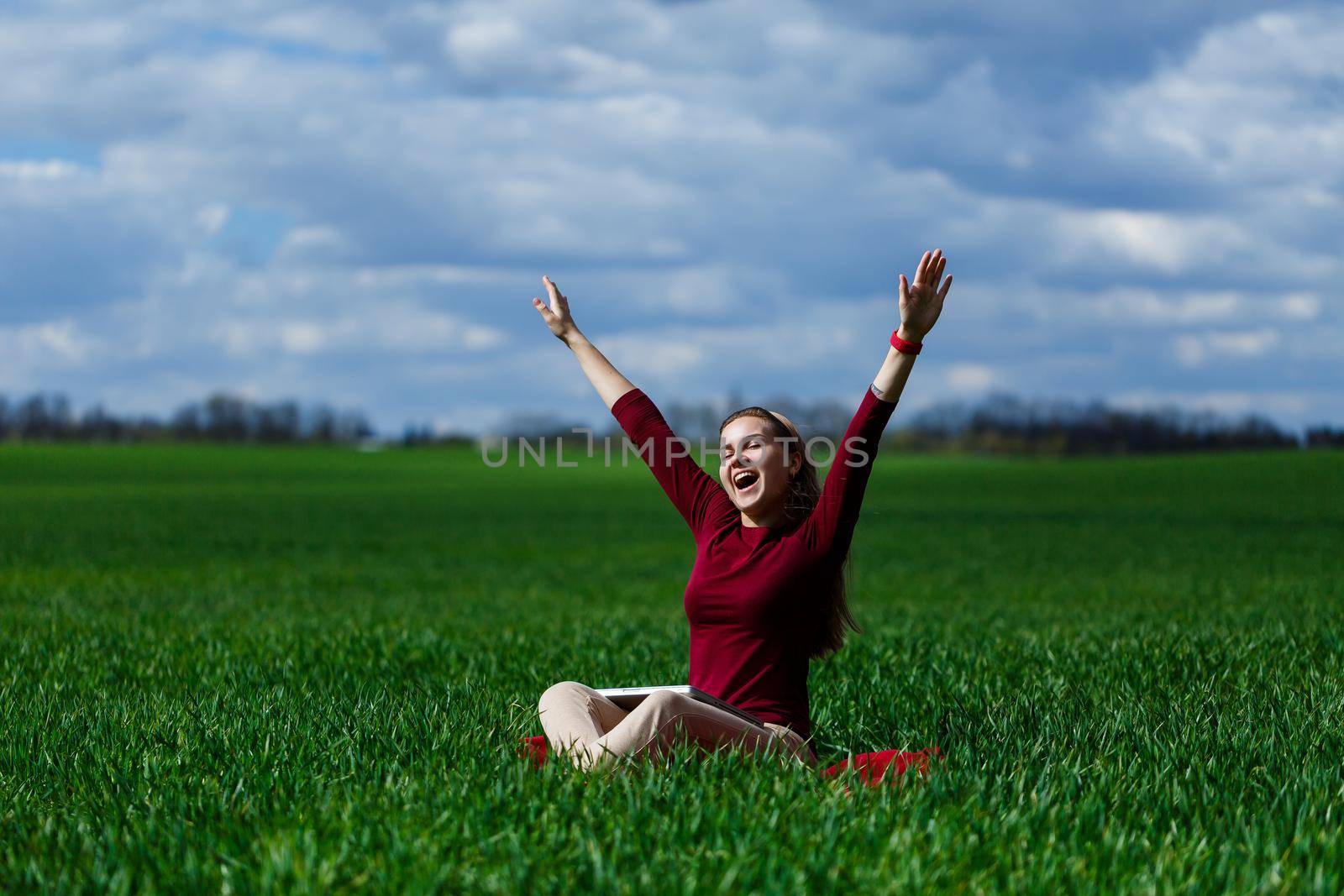 Young successful woman is sitting on green grass with a laptop in her hands. Rest after a good working day. Work on the nature. Student girl working in a secluded place. Workplace in nature