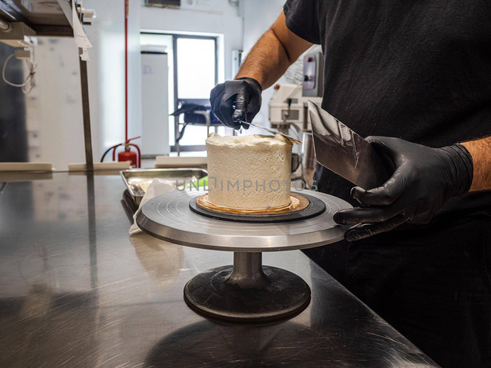 Decorator using spatula and scraper to smooth buttercream on a frosted cake